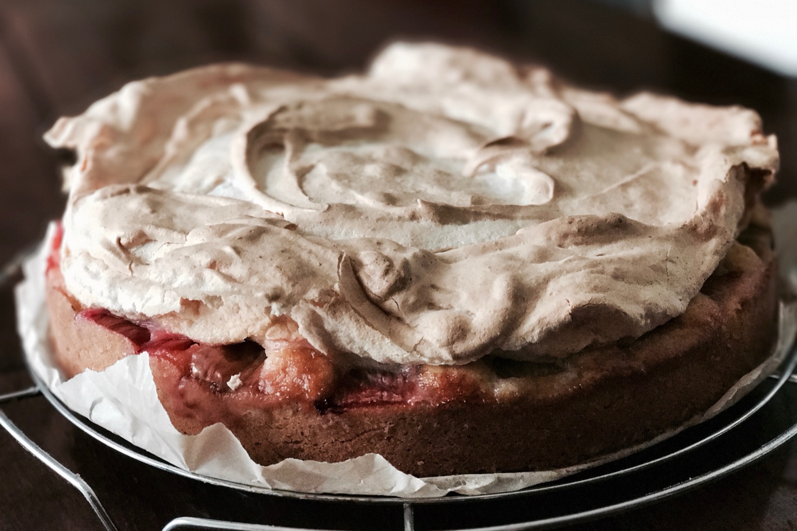 Rhubarb meringue cake with golden almond meringue on a cooling rack